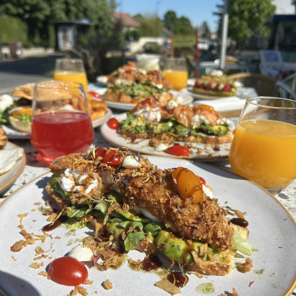 Table de brunch en terrasse avec plat salé avocat poulet croustillant, tomates cerises et jus de fruits frais, boulangerie-pâtisserie halal La manufacture du goût à Champigny-sur-Marne (94)